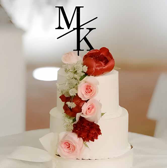 An elegant white three-tier wedding cake topped with a black acrylic cake topper featuring the initials &