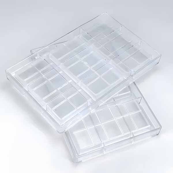 Two clear polycarbonate molds are stacked on top of each other. Each mold features multiple rectangular cavities intended for creating kunafa or chocolate desserts. The molds are transparent, allowing visibility of their interior design, which includes grid-like sections. The background is simple and light-colored, highlighting the molds.