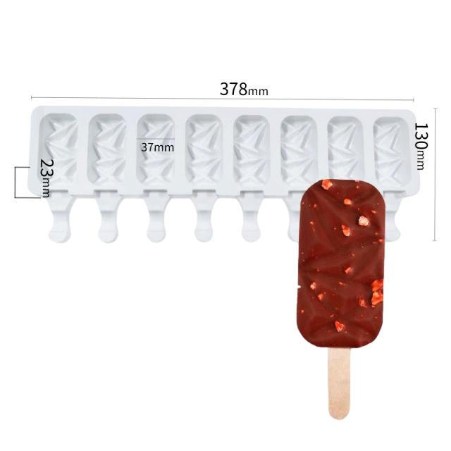 The image features a white silicone mould designed for making diamond-shaped cakesickles. The mould has eight cavities, each with a geometric pattern, and dimensions of 378mm in length, 130mm in height, and 23mm in depth. Beside the mould is a finished cakesickle, which resembles a rectangular ice cream treat with a wooden stick, coated in chocolate and sprinkled with small red pieces, likely bits of fruit or candy.