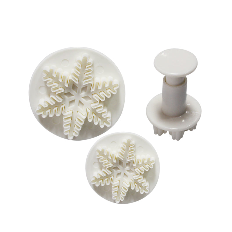 A set of three white plunger cutters shaped like snowflakes. The set includes two cutters with snowflake designs on flat circular bases and one plunger tool. The snowflake details feature intricate patterns typical of snowflakes. The cutters are arranged on a white background.