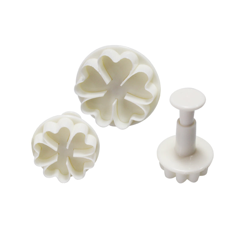 A set of three plunger cutters in the shape of heart flowers, colored white. The set includes two larger cutters with floral designs and one smaller cutter with a flower base.