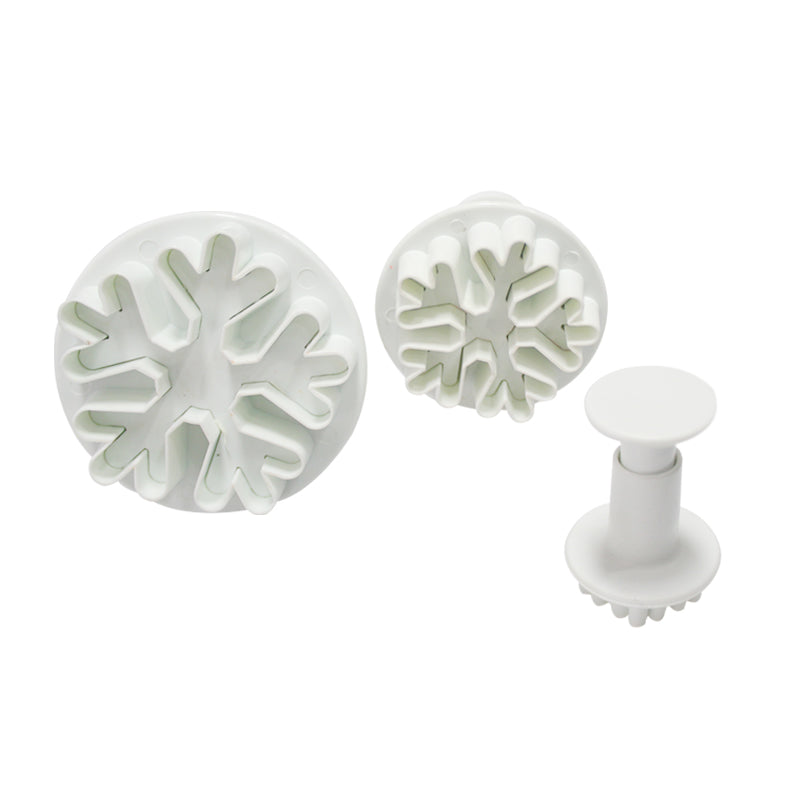 A set of three white plunger cutters designed to create snowflake shapes. Two larger circular cutters with intricate snowflake designs are positioned side by side, while a smaller cylindrical plunger cutter is placed in front. All three tools are made of plastic and have a smooth surface.