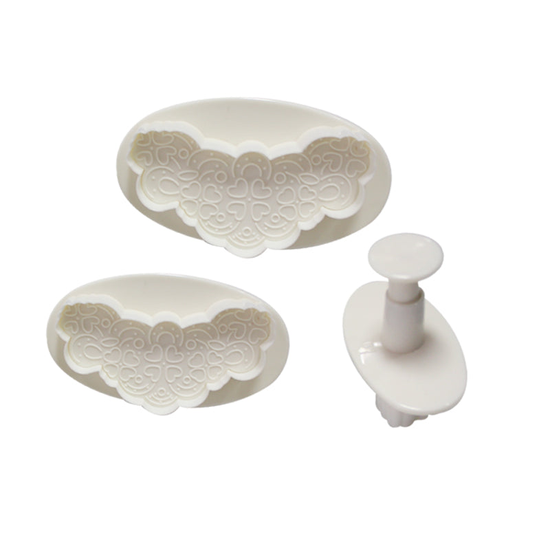 A set of three plunger cutter tools for embroidery, featuring two oval-shaped cutters with decorative heart patterns on the interior and one central plunger tool. All items are white in color, designed for creating shaped patterns in fabric.