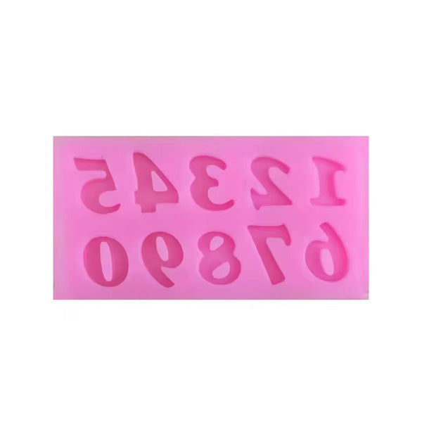 A pink silicone mould designed for crafting, featuring cut-out numbers 0 to 9 in various styles. The numbers are arranged in two rows, with the top row displaying the numbers 1, 2, 3, 4, 5, and the bottom row showing 0, 6, 7, 8, 9.