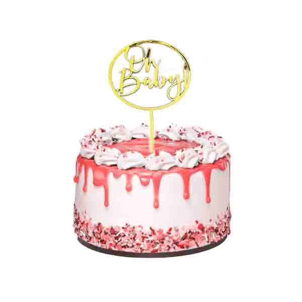 A decorated cake featuring a shiny gold acrylic topper that reads &quot;Oh Baby!&quot; The cake has a white base with pink icing drips and is topped with whipped cream and sprinkles. The sides of the cake are adorned with colorful sprinkles, creating a festive appearance.