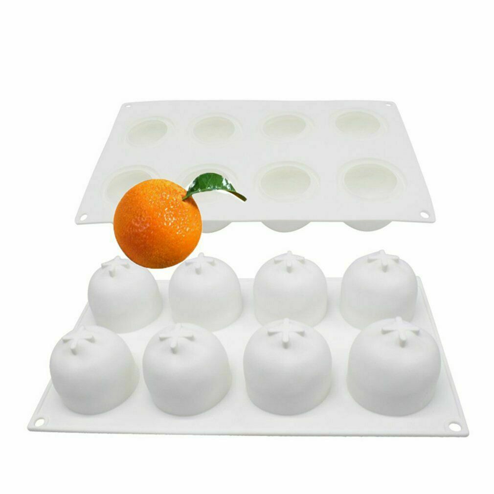 An image featuring a silicone mold designed to create 3D fruit shapes. The mold has eight cavities, each shaped like an orange with a small star detail on top. An actual orange is positioned in front of the mold, showcasing its round shape and vibrant color, complete with a small green leaf attached. The mold itself is white and flexible, ideal for making fruit-inspired edible treats.