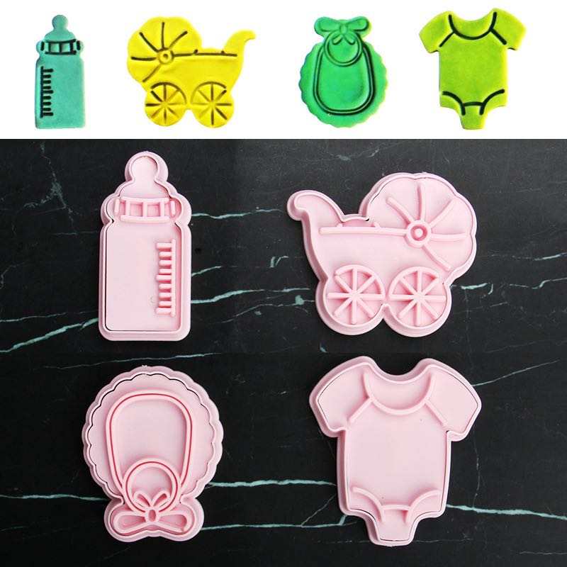 Image showing a set of four baby-themed cookie cutters. The top row features a green bottle, a yellow baby carriage, a green bib, and a yellow onesie. The bottom row displays a pink bottle, a pink baby carriage, a pink bib with a bow, and a pink onesie, all arranged on a dark surface.