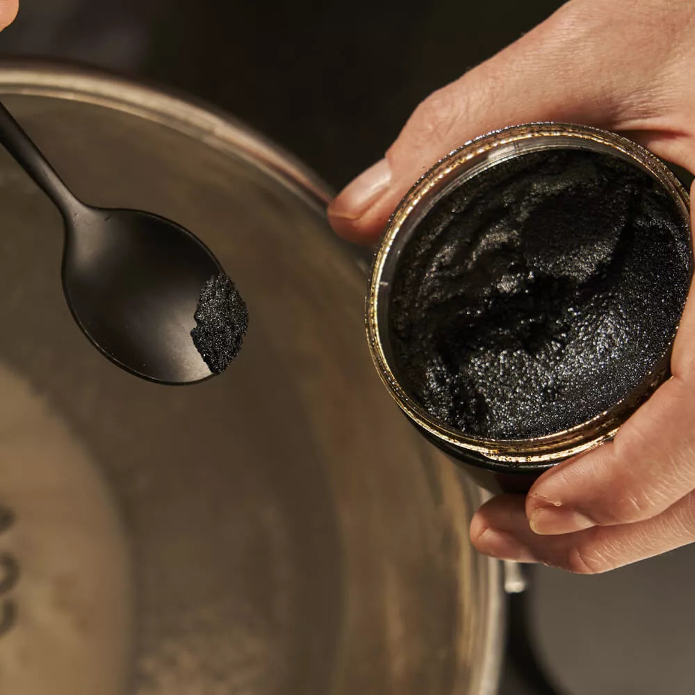 Person holding a jar of Vanilla paste with a spoon filled with the paste.