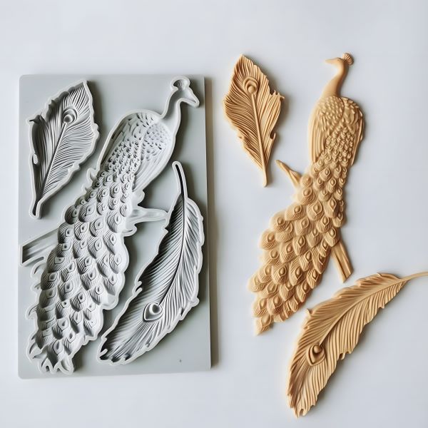 The image features a silicone mould shaped like peacocks and feathers. On the left side, there is a grey silicone mould with detailed designs of two peacocks and several feathers. To the right, there are four finished pieces made from the mould, colored in a peachy shade, depicting a peacock and multiple feather shapes. The overall composition highlights the intricate designs and textures of the mould and the produced items.