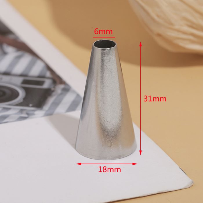 A metal piping nozzle is displayed upright on a light-colored surface. The nozzle has a conical shape with a top opening measuring 6mm in diameter and a wider base with an 18mm diameter. The total height of the nozzle is 31mm. The background features a partially visible patterned fabric and a camera, adding context to the scene.