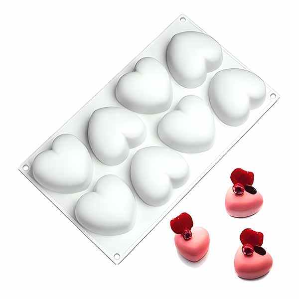 A white silicone mould featuring eight heart-shaped cavities is shown at the top of the image. Below the mould, there are three heart-shaped decorations: two pink and one red, each topped with a cherry-like ornament. The mould and decorations are arranged on a white background.