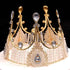 A decorative cake topper designed to resemble a tiara or crown. It features a golden metallic frame with intricate detailing, including several peaks adorned with clear gemstones and pearl-like elements. The base has a lace-like pattern, embellished with sparkling crystals and beads. The overall look is elegant and royal, suitable for celebratory cakes or special occasions.