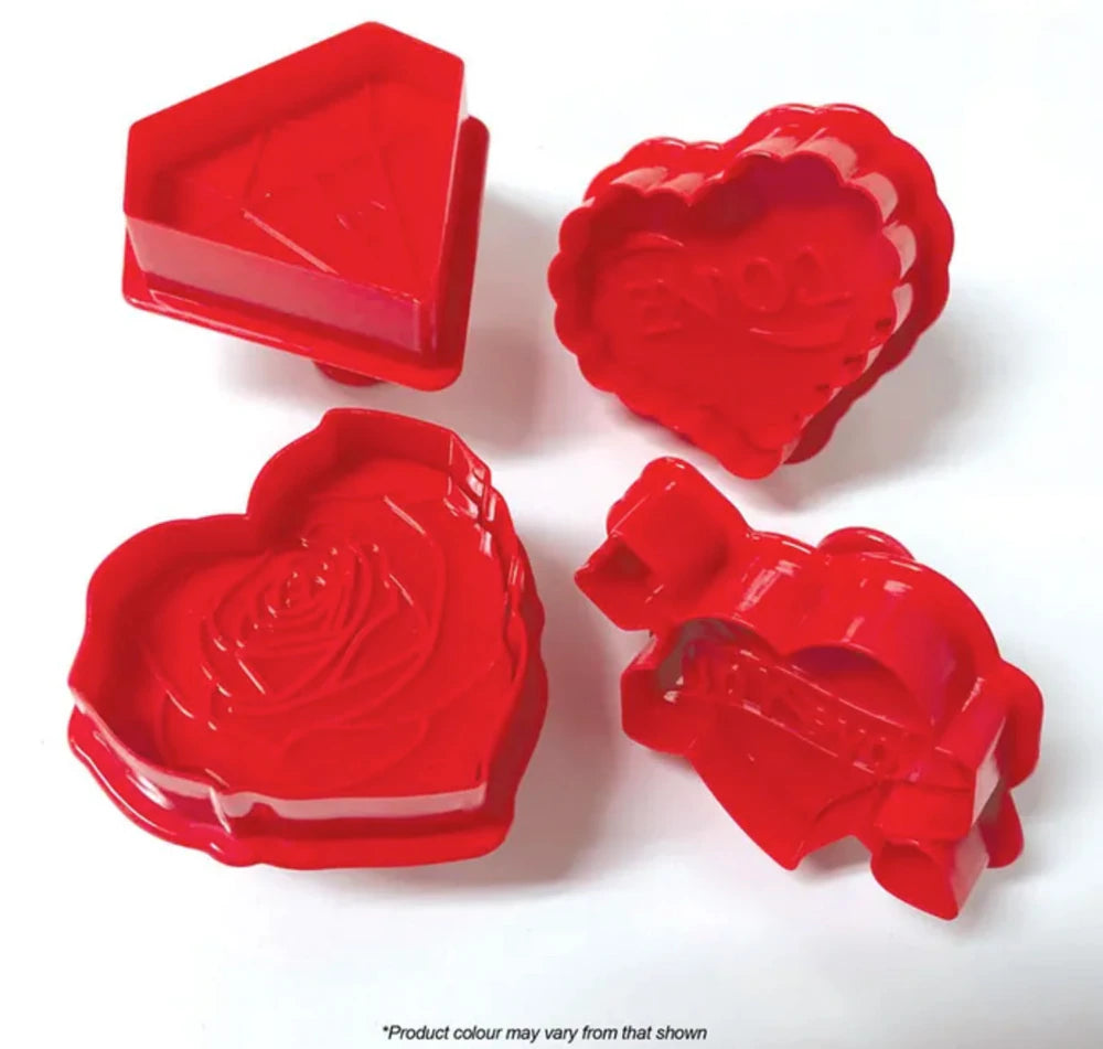 The image features a set of four red plunger cutters designed for baking or crafting. The cutters include shapes such as a diamond, a decorated heart with the word &quot;LOVE,&quot; a heart featuring a rose design, and another heart with a decorative edge. All items are bright red and made of plastic, showcasing various detailed designs suitable for creating themed decorations or cookies.