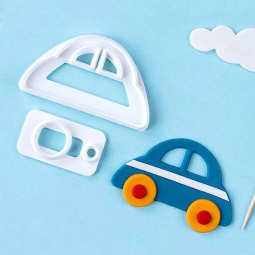 A light blue background features three items related to baking. There is a white cookie cutter in the shape of a car and a smaller rectangular cutter, both made of plastic. Next to them, there is a completed cookie shaped like a blue car with white stripes and small yellow and red wheels. A white cloud shape is also visible in the background.