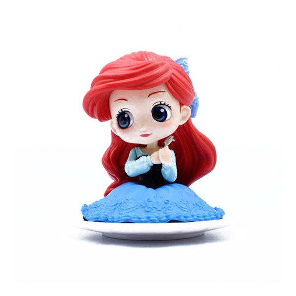 A colorful figurine of a mermaid character with large, expressive eyes and vibrant red hair, styled with a blue bow. She wears a light blue top and a flowing blue dress adorned with intricate patterns. The figurine is set on a white circular base, giving it a playful and whimsical appearance, suitable as a cake topper.