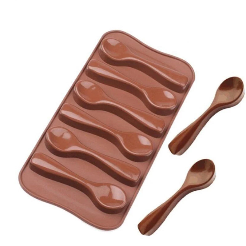 A brown silicone mold containing six spoon-shaped depressions for making small spoons. Two additional brown spoon-shaped chocolates are placed alongside the mold, showing the end result of the mold&