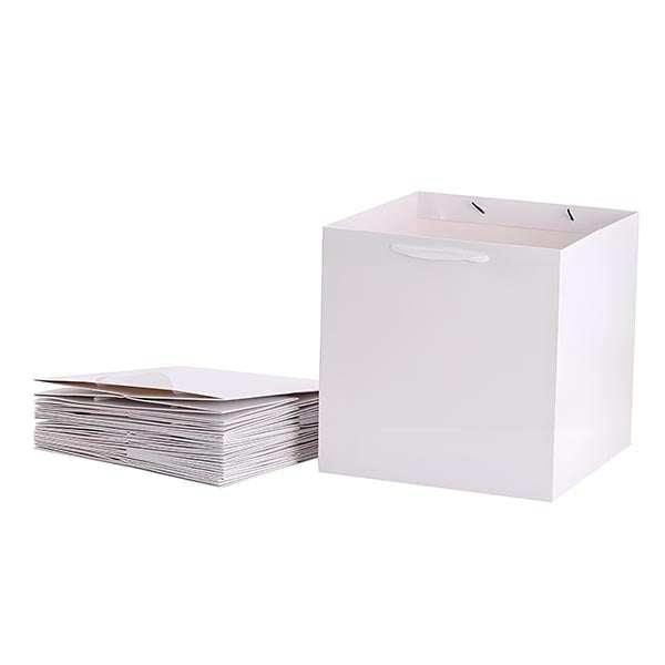 A stack of white kraft square paper bags and a matching square container. The bags are neatly arranged in a pile on the left, while the container on the right is open at the top, featuring two handles. The entire setup is on a plain background.