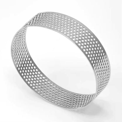 This image features a stainless steel perforated tart ring. The ring has a round shape with a diameter of 8 cm and a height of 2 cm. It is constructed from stainless steel and features numerous small holes evenly distributed throughout its surface, allowing for even cooking and airflow. The ring is set against a plain light background, highlighting its shiny metallic finish.