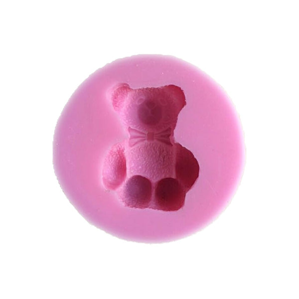 A circular silicone mould in a soft pink color, featuring an embossed design of a teddy bear wearing a bow tie. The teddy bear has a textured surface and is centrally positioned within the mould.