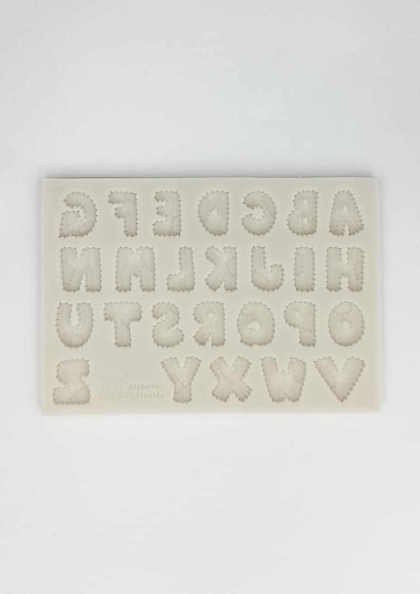 A silicone alphabet mold displaying uppercase letters A to Z, featuring a funky design with jagged edges. The letters are arranged in four rows, with numbers 0 to 2 included. The mold is cream-colored and set against a plain white background.