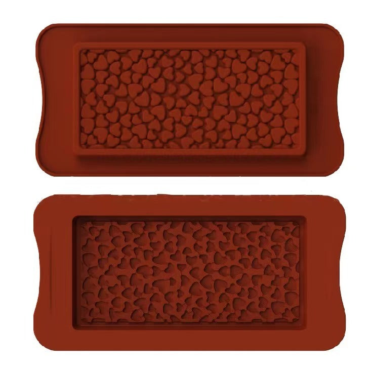 The image shows two silicone moulds for making chocolate bars, both designed with a pattern of small hearts. The moulds are rectangular in shape, with rounded edges and a textured heart design covering the surface. The top mould is positioned above the bottom mould, and both have a similar heart pattern, creating a decorative effect for the chocolate bars. The colour of the moulds is a rich, reddish-brown.