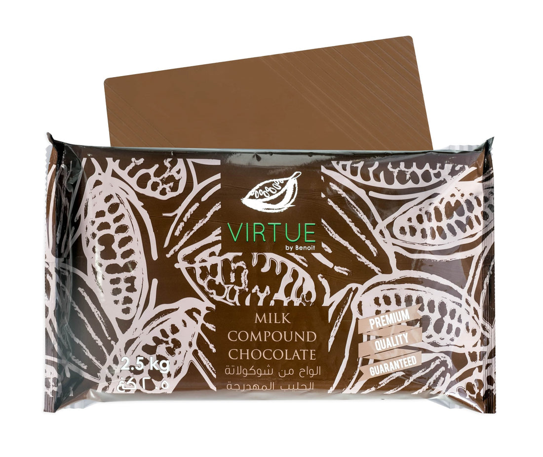 A 2.5 kg package of Virtue milk chocolate compound. The packaging features a brown background with white cocoa bean illustrations. The product name &quot;VIRTUE&quot; is displayed prominently in green, along with the text &quot;MILK COMPOUND CHOCOLATE&quot; in white. There are also labels indicating &quot;PREMIUM,&quot; &quot;QUALITY,&quot; and &quot;GUARANTEED.&quot; An additional piece of chocolate can be seen partially above the package.