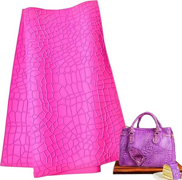 A bright pink crocodile alligator pattern impression mat is displayed upright next to a purple handbag with a similar texture. Both items are on a wooden surface, alongside a plate with a slice of cake, and a small cup. The impression mat showcases a textured pattern resembling reptile skin.