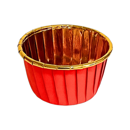 Red pleated cup with a gold interior and rim, set against a black background. The shiny surface and warm colors create an elegant, festive tone.