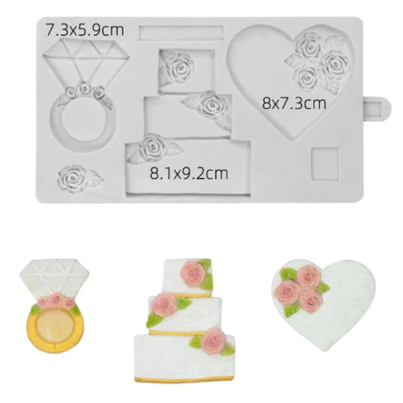 A silicone mould featuring various shapes related to weddings. The mould is gray and includes a diamond ring, a three-tier wedding cake, and a heart shape, each adorned with rose designs. The dimensions of each item are indicated on the mould: the diamond ring is 7.3x5.9 cm, the wedding cake is 8.1x9.2 cm, and the heart shape is 8x7.3 cm. Three decorative pieces made of icing are displayed below the mould: a diamond ring, a three-tier cake, and a heart with roses.
