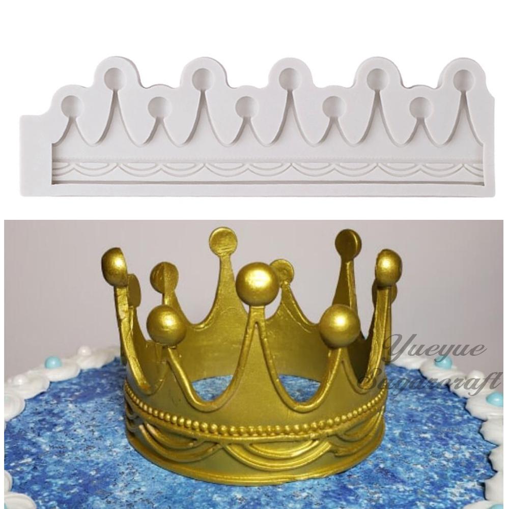 The image shows two items related to cake decoration. The top part features a white silicone mold shaped like a crown, with decorative peaks and grooves. The bottom part displays a golden crown made of fondant, placed on a cake with a blue, sparkly surface and white icing accents. The crown has several round balls and pointed peaks, enhancing its regal appearance.