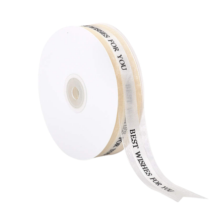 A roll of white ribbon is displayed, measuring 2.5 cm in width and 5 yards in length. The ribbon features the text "BEST WISHES FOR YOU" printed along its length in a decorative font. The roll is positioned so that part of the ribbon is unraveling, showcasing the printed message.