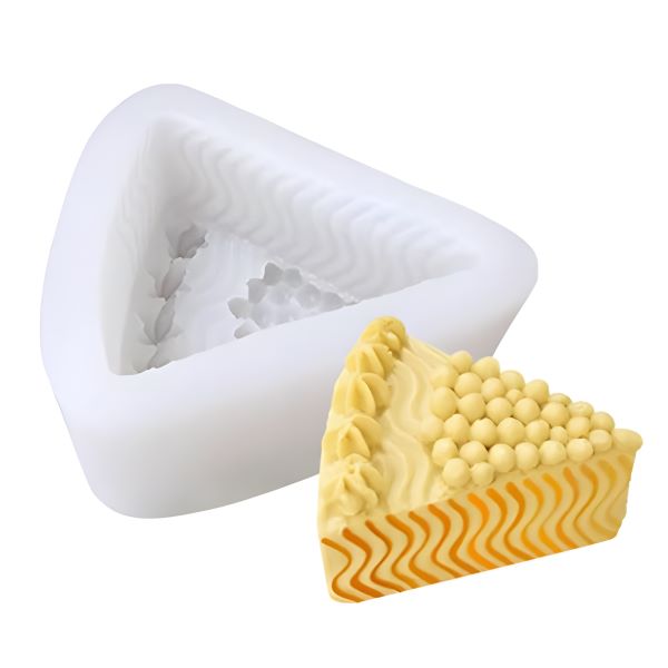 A triangular silicone mold designed to create cheese-shaped items, with a textured interior. Next to the mold, there is a finished cheese-shaped product that resembles a wedge of cheese, featuring a creamy yellow hue, decorative dots, and a wavy orange stripe along the bottom. The mold appears flexible and is white in color.
