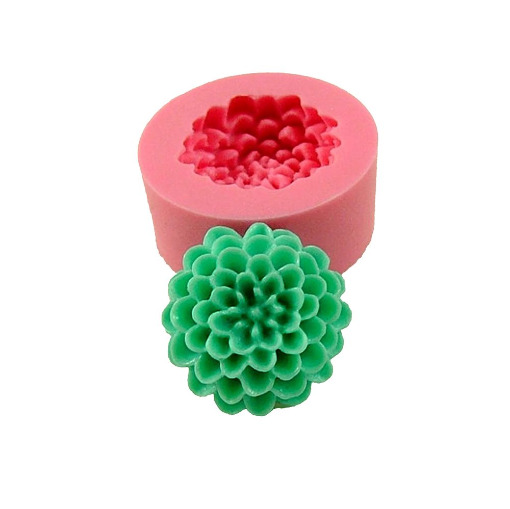 A pink silicone mold in the shape of a flower with a detailed green flower-shaped candle made from the mold placed in front.