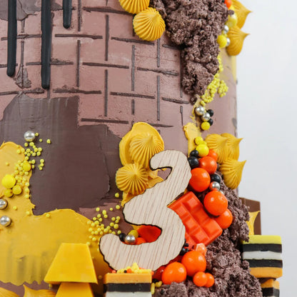 Close-up of a decorative cake featuring a textured brown and yellow design, a wooden number 3, and colorful candy accents, creating a festive atmosphere.