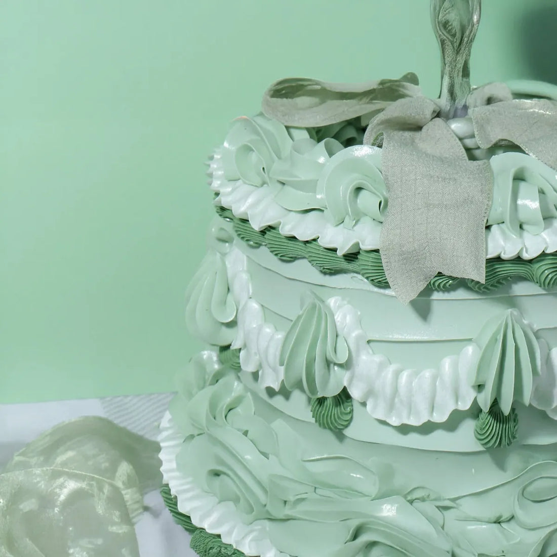 Pale green, intricately decorated cake with white frosting swirls and frills. A silver bow sits on top, creating a festive, elegant appearance.