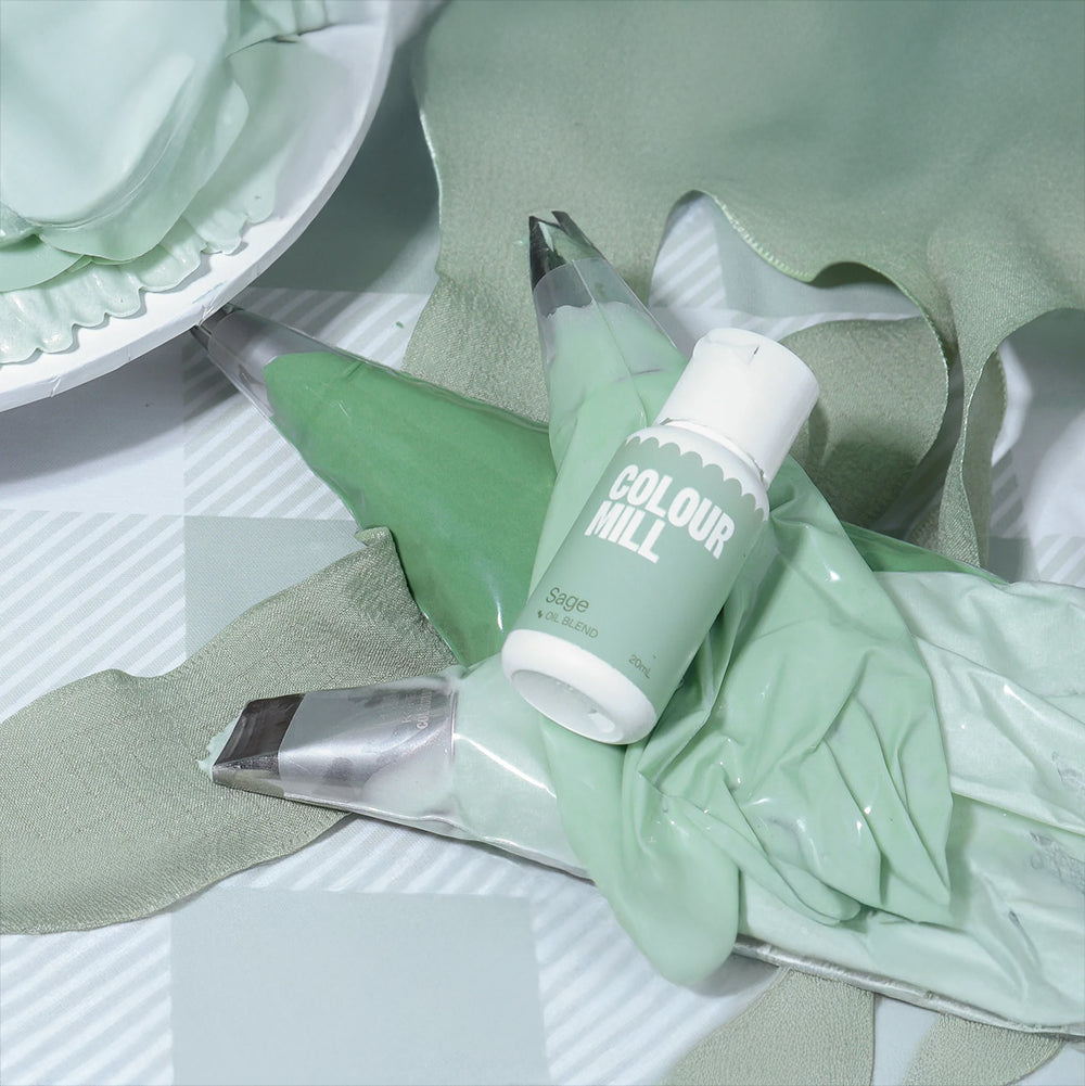 Sage-green cake decorating supplies, including three piping bags and a small bottle of food coloring labeled "Colour Mill Sage," on a patterned surface.
