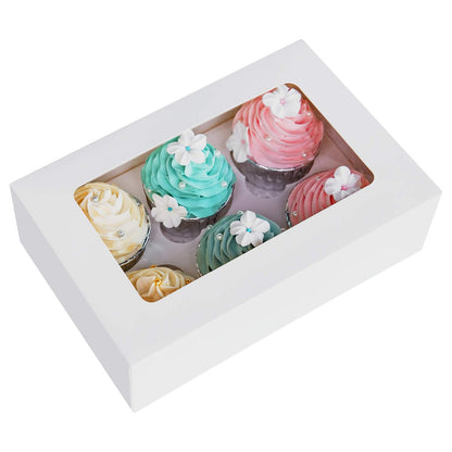 A white cupcake box containing six cupcakes is shown. The box features a clear window on the top, allowing a view of the cupcakes inside. The cupcakes have decorative frosting in pastel colors: two pink, two blue, one yellow, and one purple. Each cupcake is topped with small white flowers and embellishments, including tiny pearls. The overall presentation is cheerful and suitable for a special occasion.