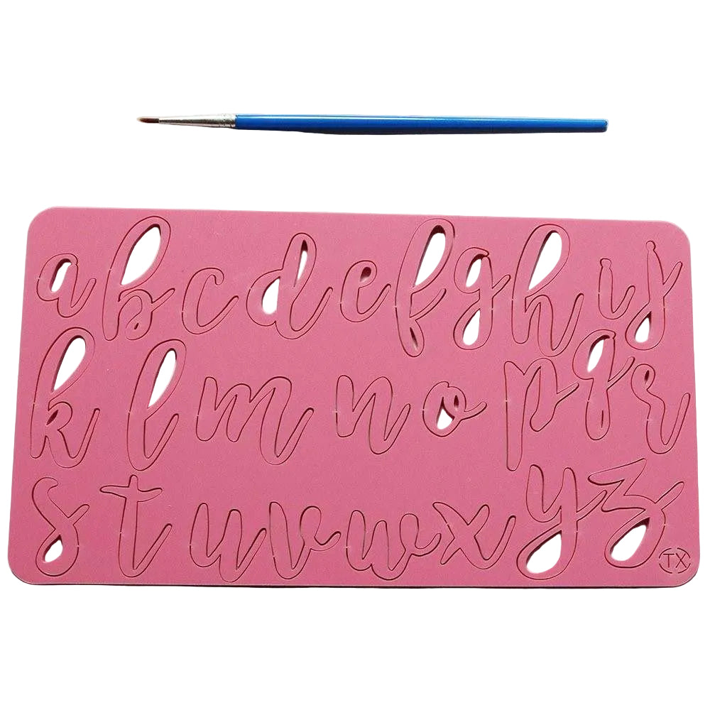 The image features a pink acrylic cake stamp with lowercase letters of the alphabet, designed in a cursive style. The letters are cut out of the stamp for easy use in cake decorating. A small blue paintbrush is positioned above the stamp, indicating that it may be used for filling the letters with icing or paint. The background is a light color, providing contrast to the pink stamp.