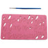 The image features a pink acrylic cake stamp with lowercase letters of the alphabet, designed in a cursive style. The letters are cut out of the stamp for easy use in cake decorating. A small blue paintbrush is positioned above the stamp, indicating that it may be used for filling the letters with icing or paint. The background is a light color, providing contrast to the pink stamp.