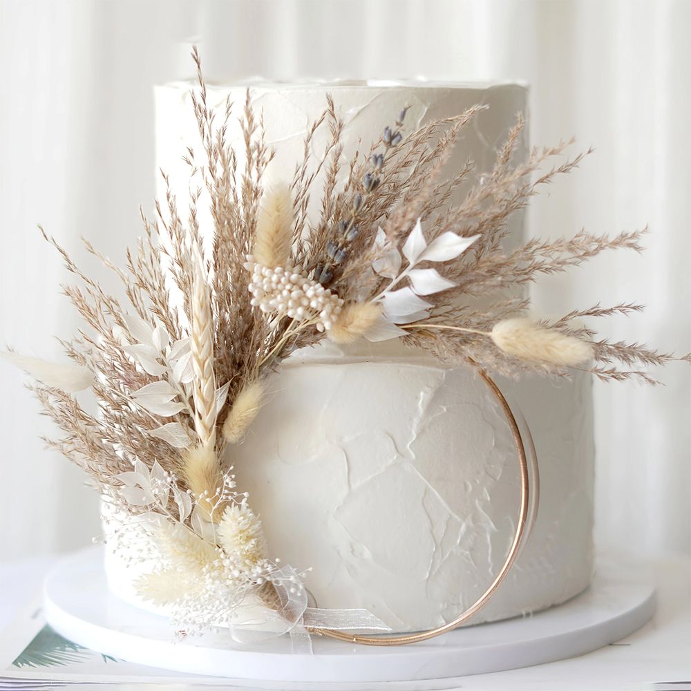 A beautifully decorated white wedding cake featuring dried grass and flowers, perfect for a natural-themed wedding.