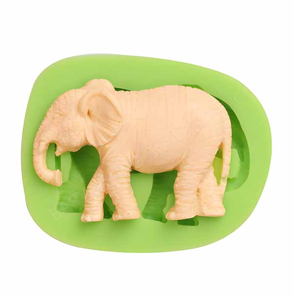 A green silicone mold in the shape of an elephant is shown, with the molded elephant figure inside. The elephant has a light beige color and detailed textures representing its skin and features. The mold is flexible and designed for creating elephant-shaped treats or decorations.