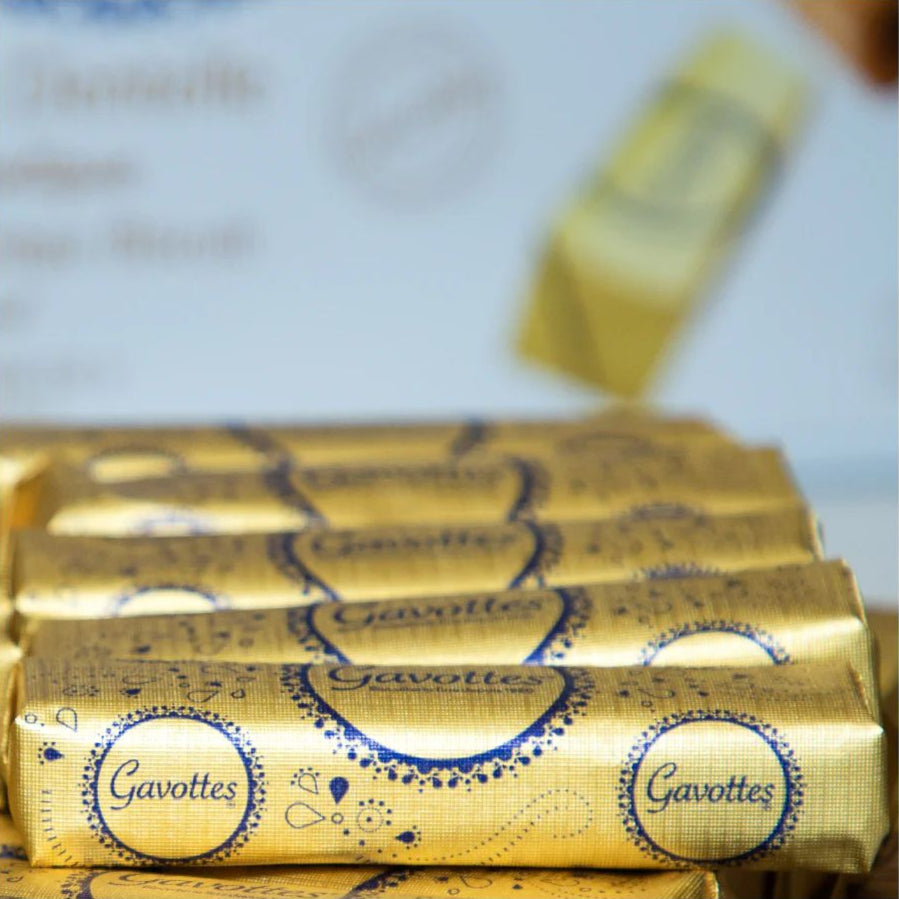 Golden-wrapped Gavottes cookies are neatly stacked in rows, displaying ornate blue designs and brand logos, conveying elegance and indulgence.
