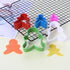 A set of five gingerbread man cookie cutters in various colors is displayed on a cooling rack. The cutters include red, blue, pink, green, and white. There are also two shaped cutouts in orange and yellow on a pale yellow surface next to the cutters. The arrangement showcases the playful design of the cookie cutters, ideal for making gingerbread man cookies.