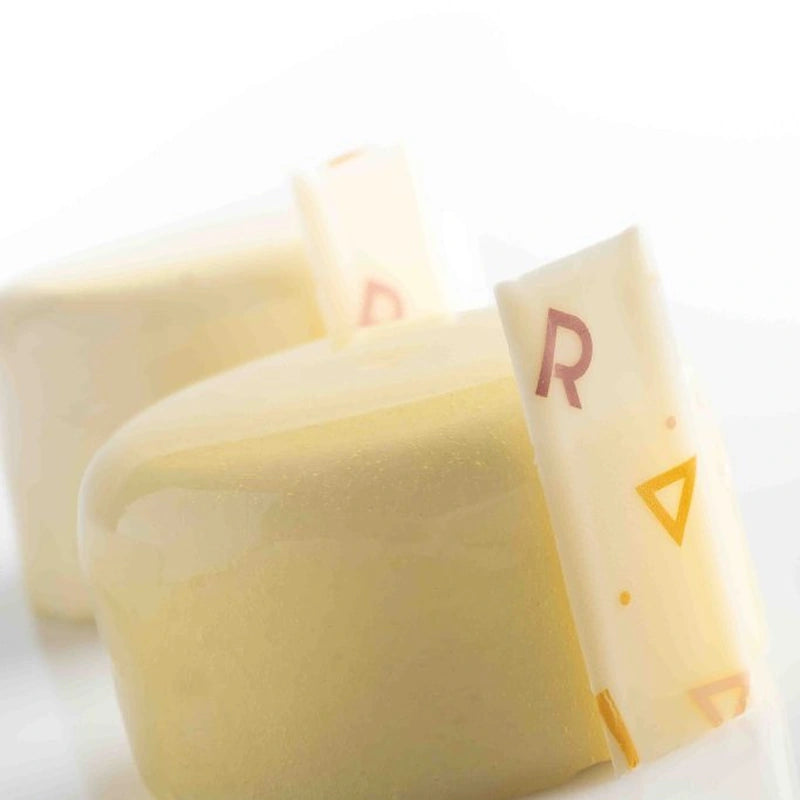 Two pieces of cheese partially covered by a white wrapper, placed on a neutral background.