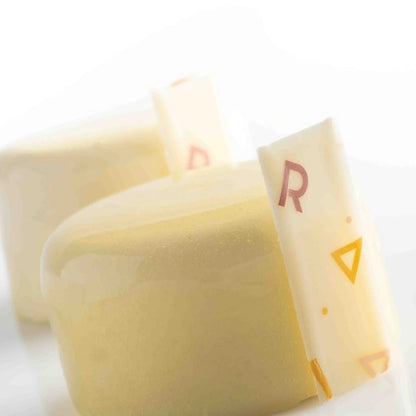 Two pieces of cheese partially covered by a white wrapper, placed on a neutral background.