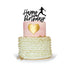 A two-tier birthday cake featuring a pink top tier with a gold heart design, and a bottom tier decorated with white ruffles and gold accents. Atop the cake is a black custom cake topper that reads "Happy Birthday" with a silhouette of a soccer player in action. The cake is presented on a circular white plate against a white background.