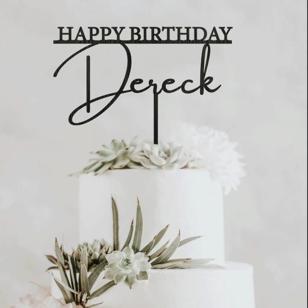 A white multi-tier cake decorated with succulents and flowers, topped with a black acrylic cake topper that reads &quot;HAPPY BIRTHDAY&quot; above the name &quot;Dereck.&quot; The backdrop is light and neutral, enhancing the decorative elements of the cake and topper.