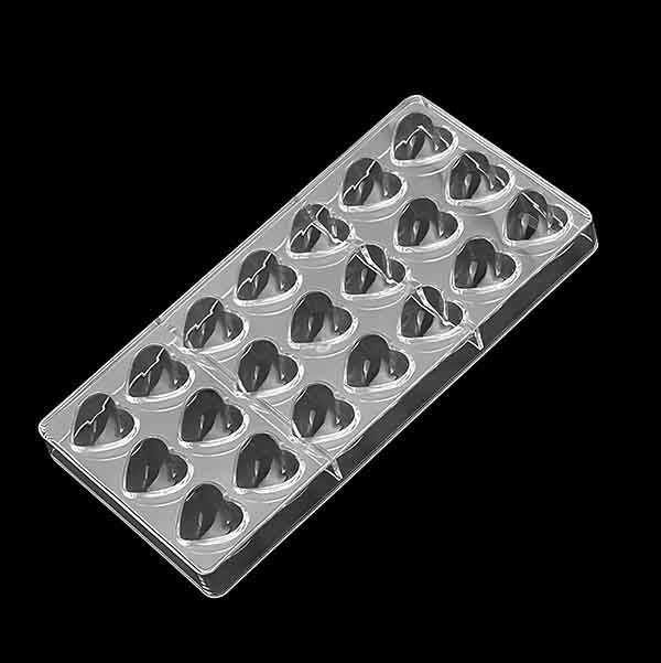 A clear plastic chocolate mold designed in the shape of hearts, featuring multiple cavities arranged in a grid pattern. Each cavity is heart-shaped, suitable for making heart-shaped chocolates. The background is solid black.