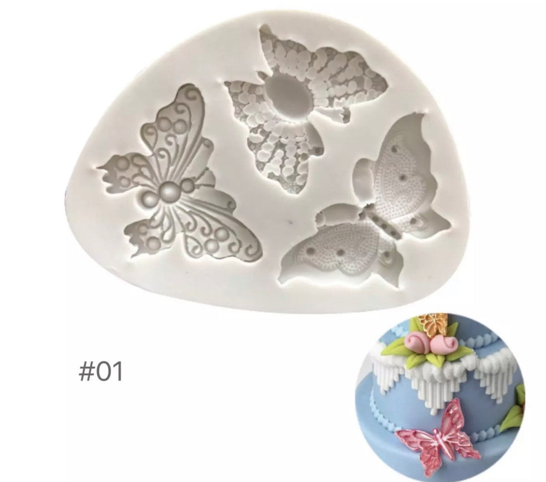A white silicone mould shaped like an irregular oval, featuring three detailed butterfly designs in relief. One butterfly has intricate swirls and dots, another has a floral pattern, and the third features fine lace-like details. Below the mould, there is a small image of a decorated cake that features a pink butterfly made from the mould, along with decorative flowers and leaves. The mould is labeled with the number "