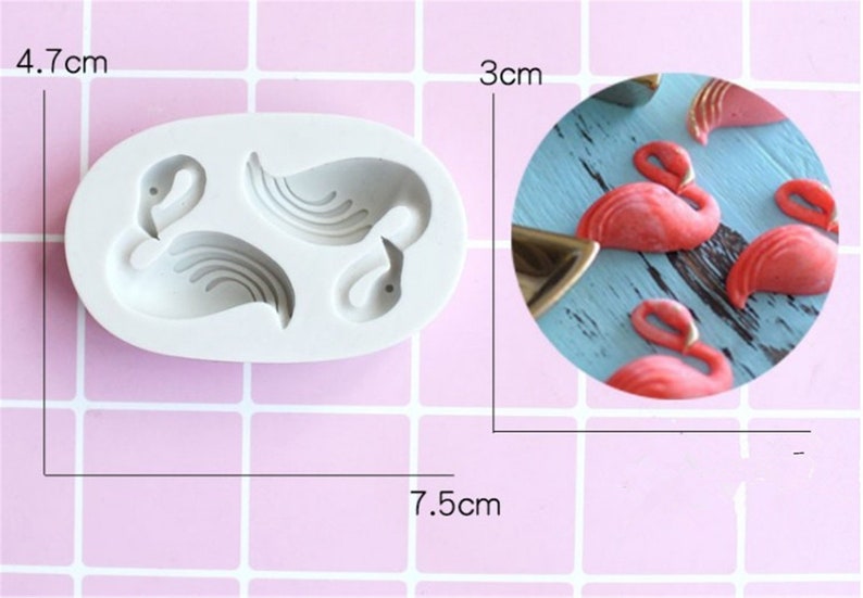 An oval-shaped silicone mold with two flamingo designs, measuring approximately 7.5 cm by 4.7 cm. The mold is light gray and features detailed outlines of the flamingos. An inset image shows small, pink flamingo-shaped decorations made from a separate material, arranged on a light blue wooden surface. The decorations are about 3 cm in height. The background of the main image has a pastel grid pattern.